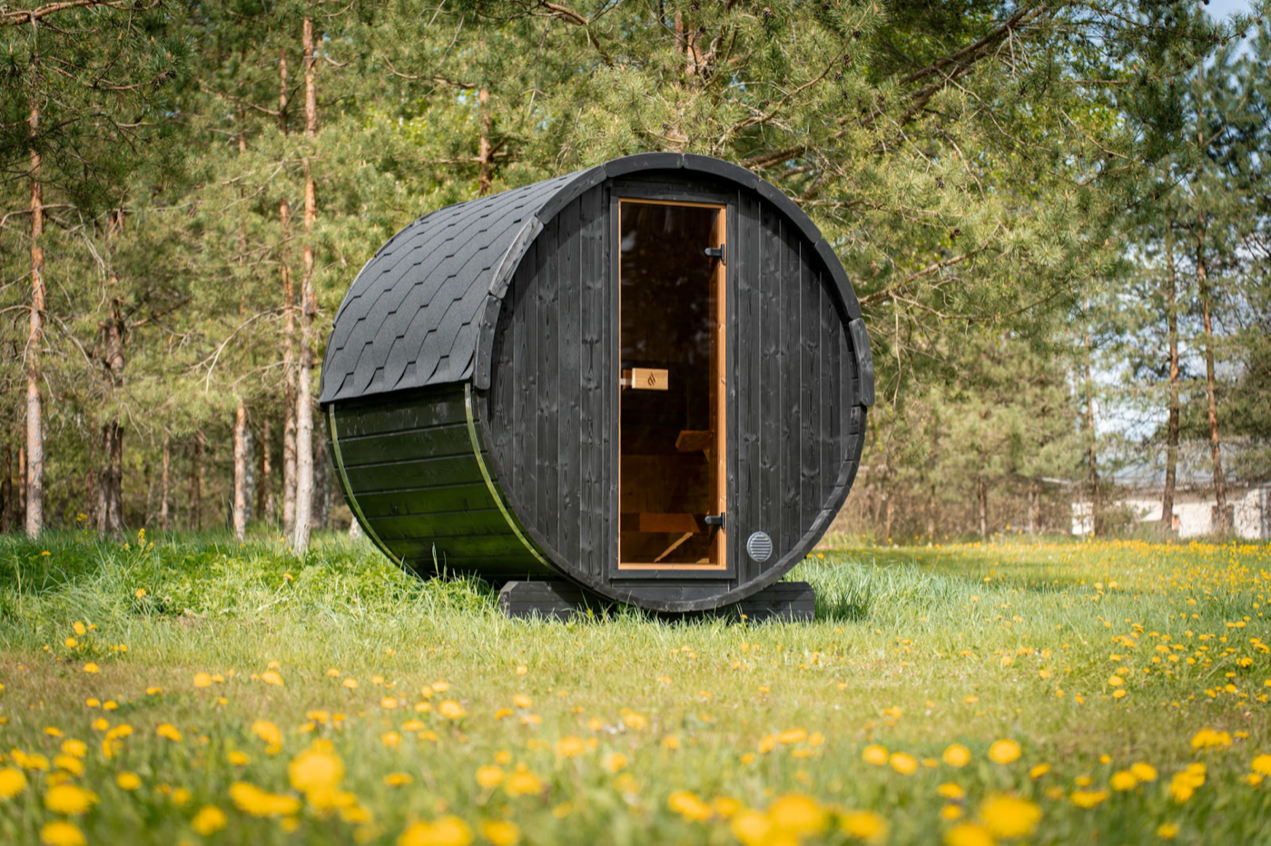 PlusLife Cove Barrel Sauna, a black stained timber barrel cabin with a shingled roof and a timber framed glass door