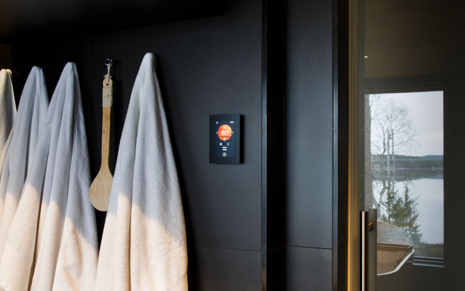 Harvia Wi-Fi control panel on a dark sauna wall beside hanging towels and a window