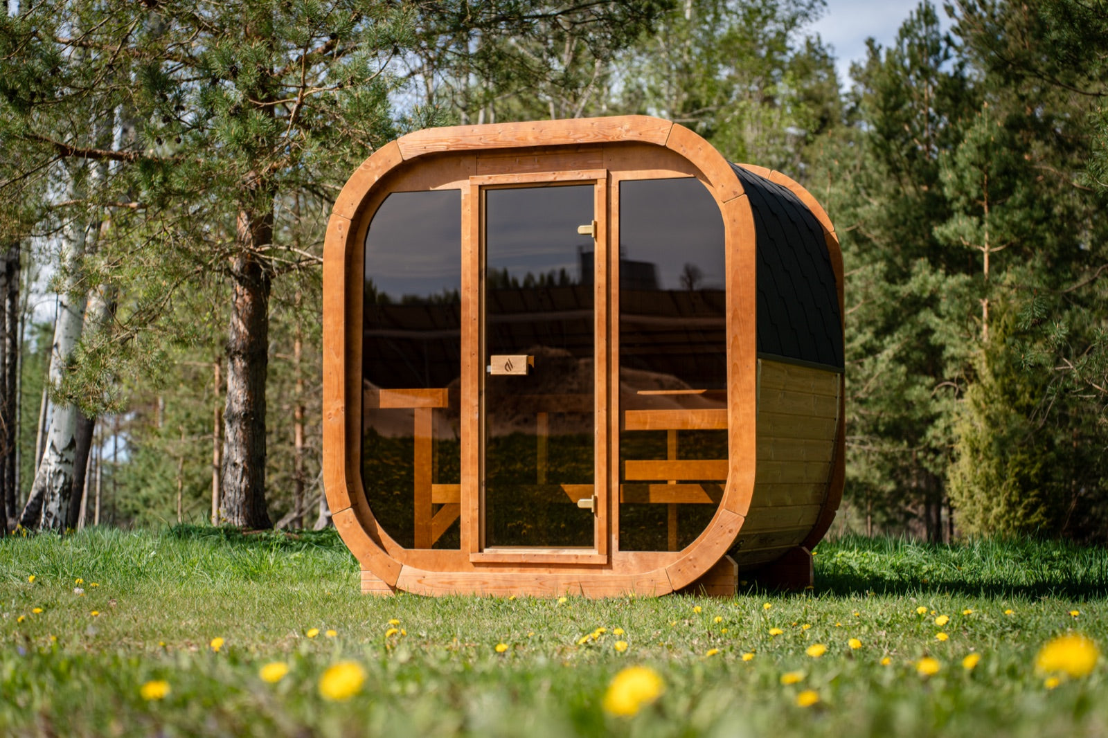 Max Traditional Sauna 2.0 with its full glass front, standing on grass in a birch forest