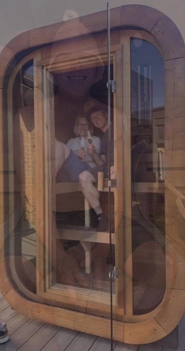 Two people sitting inside a timber sauna, seen through its glass door
